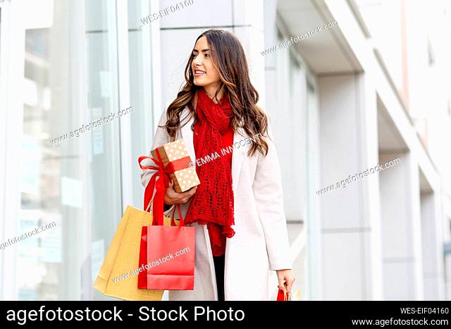 Young woman with Christmas present and shopping bags walking by building