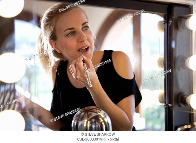 Woman applying lipstick using mirror