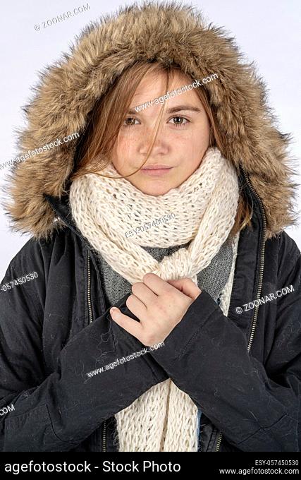 A beautiful blonde teenage model posing with a winter coat in a studio environment