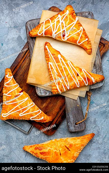 Apple and cinnamon turnovers are served on a wooden serving board with a textured concrete background. Top view, flat lay
