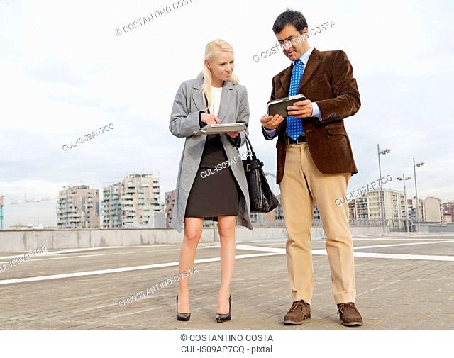 Businessman and businesswoman outdoors, holding digital tablets, sharing information