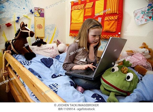 Girl, 7 years old, working with a computer at home in her room, sitting on her bunk bed, doing homework for school, educational software