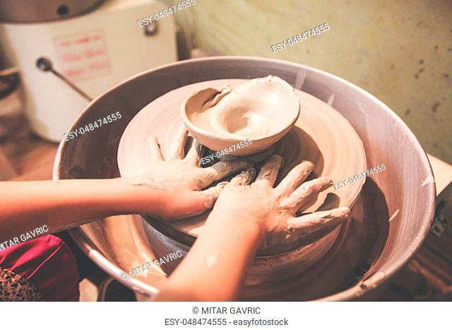 Child hands shaping clay on pottery wheel at workshop