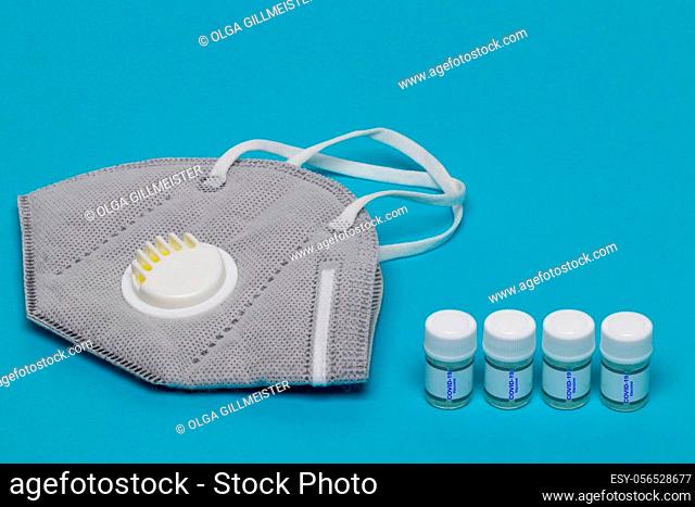 Coronavirus treatment concept. Close-up of a N95 face mask or particle filtering half mask and four ampoules Covid-19 vaccine on a blue background