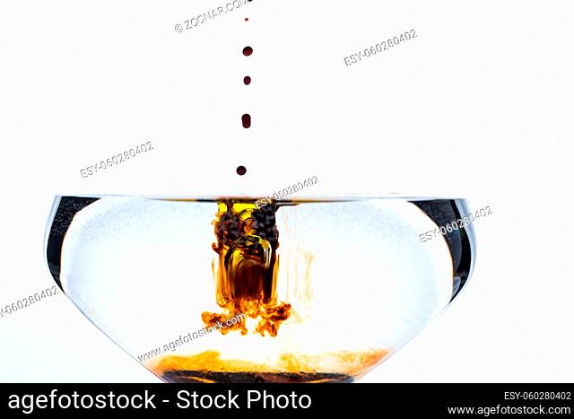 Detail of drops of dark brown balsamico vinegar dripping into glass of water isolated on white background