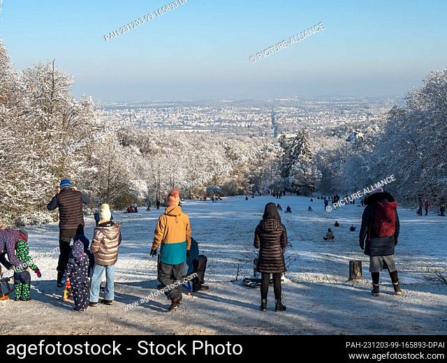 03 December 2023, Baden-Württemberg, Stuttgart: People enjoy the sunny winter weather and toboggan down a slope at Solitude Palace
