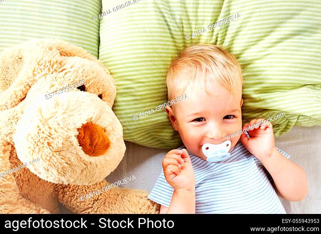 One year old baby lying in the bed with green bedding with soft toy