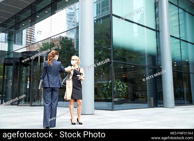 Business people wearing face mask greeting with elbow bump against office building