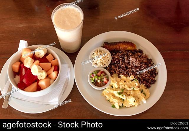 Gallo pinto breakfast served on the table with a fruit salad, Traditional gallopinto dish with fried eggs and a bowl of fruit salad on the table
