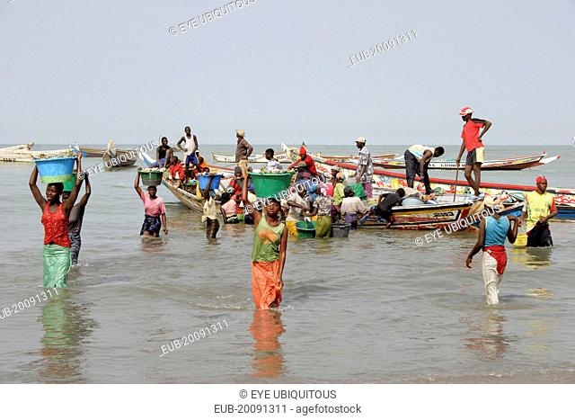 Tanji coast. Women carrying bowls full of fish on their heads through shallow water from fishing boats to the beach and fish market