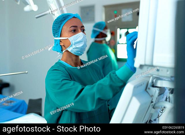 Biracial female surgeon operating computerised medical equipment in operating theatre