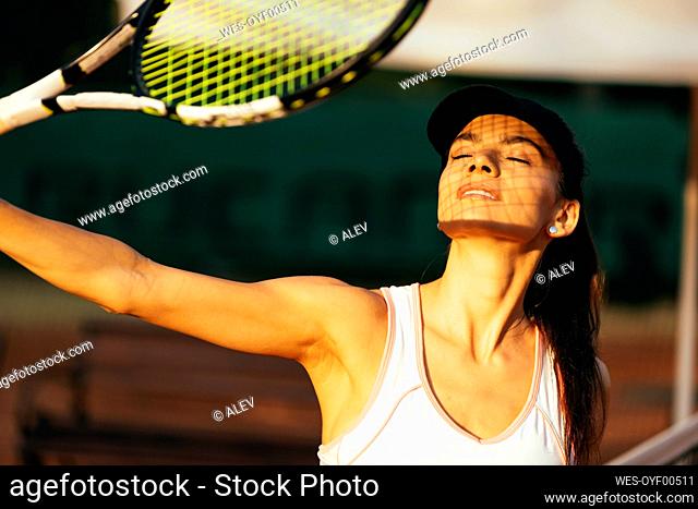 Female tennis player with eyes closed holding racket