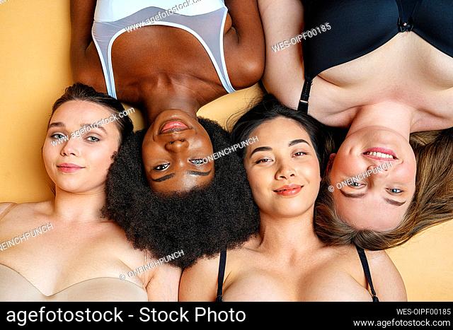 Friends smiling while lying on yellow background