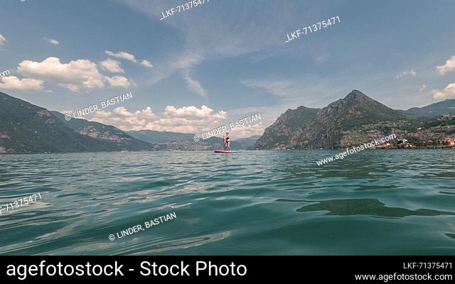 Woman paddles on SUP board in front of mountains in Lake Iseo in Italy