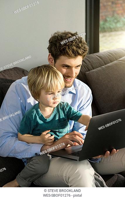Father and son looking at laptop on couch at home