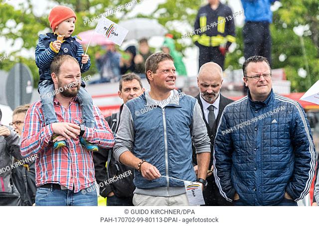 Former professional cyclist Jan Ullrich stands on the sidewalk holding a flag with the inscription ""on tour"" and awaits with fans for the arrival of the...