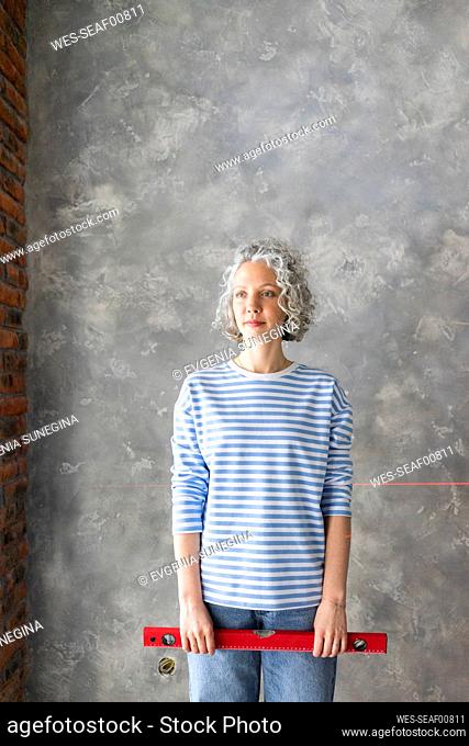Woman with level measuring tool standing in front of gray wall