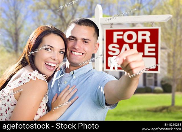 mixed-race excited military couple in front of new home with new house keys and for sale real estate sign outside