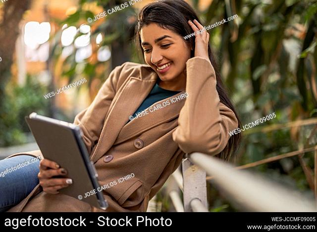Happy woman using tablet PC sitting by railing