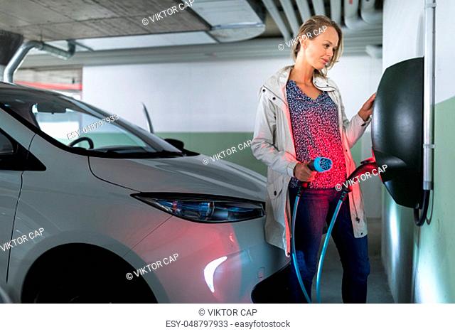 Young woman charging an electric vehicle in an underground garage equiped with e-car charger. Car sharing concept
