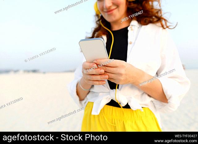 Smiling woman text messaging through smart phone at beach