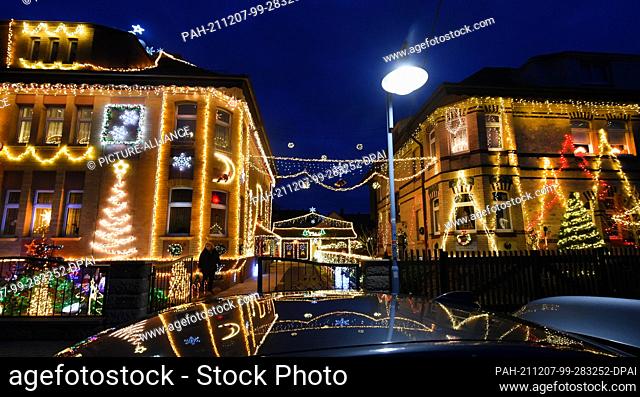 03 December 2021, Saxony, Borsdorf: The two Christmas-decorated house fronts of the Papenfuß (l) and Mauersberger families are reflected on a car roof