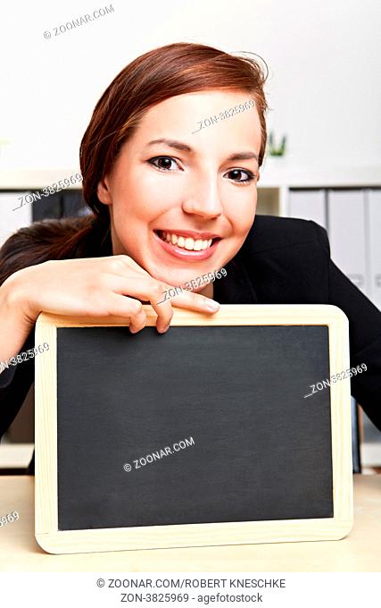 Lächelnde Geschäftsfrau sitzt mit leerer Schiefertafel am Schreibtisch