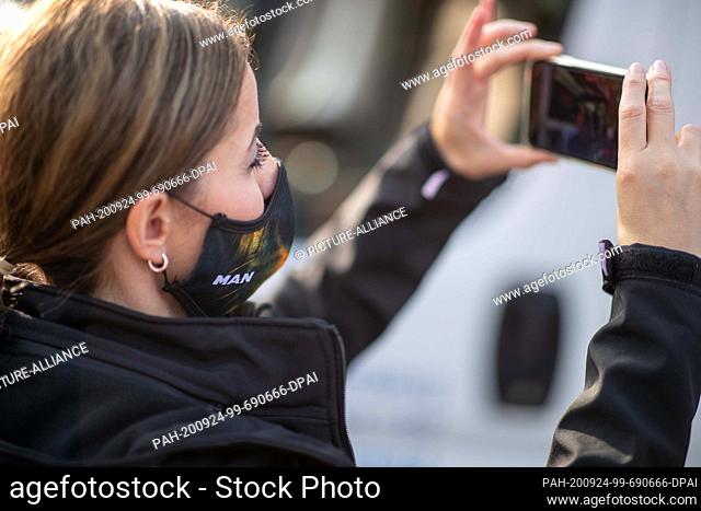 24 September 2020, Bavaria, Nuremberg: An employee of the truck manufacturer MAN in Nuremberg films with her mobile phone a protest against a planned job...