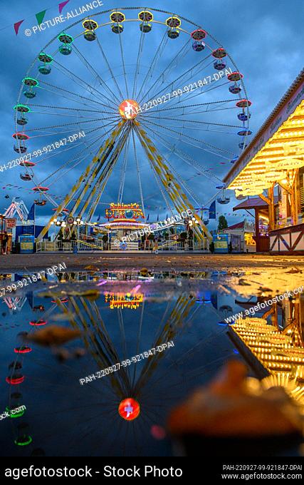 27 September 2022, Saxony-Anhalt, Magdeburg: The Ferris wheel of the Autumn Fair 2022 is reflected in the evening in a rain puddle in which already autumnal...