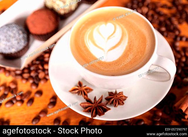 Close-up of a Cup of latte or cappuccino with latte art. Coffee on a wooden table with scattered coffee beans, anise and cinnamon lying on a saucer