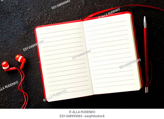 Empty red notebook with red pen and headphones on dark background. Blank paper for text. Flat lay, top view, copy space
