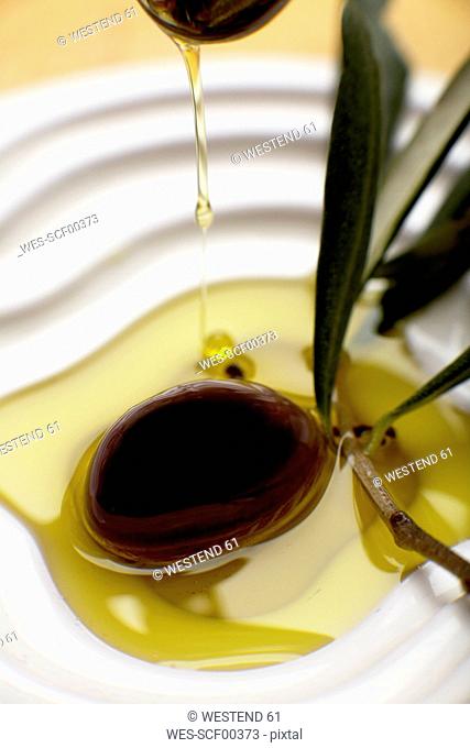Olive oil poured over olive, elevated view, close-up