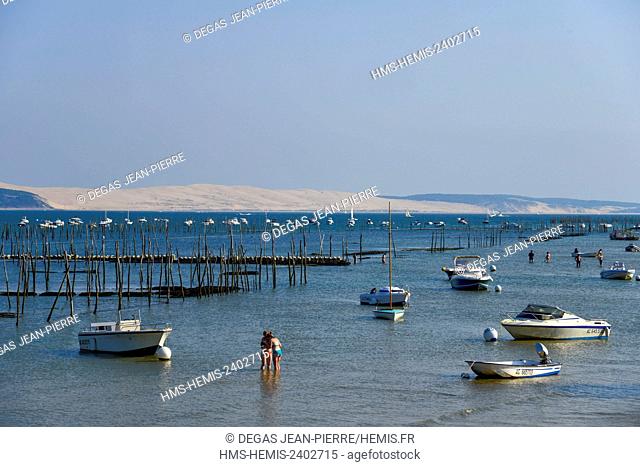 France, Gironde, L'Herbe, Young womens in the water in the middle of boats with oyster beds and the Pyla Dune in the background