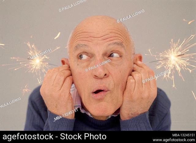 Man holds star thrower to his ears, gray background, blue shirt