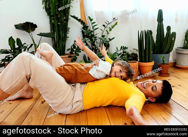Smiling son with arms outstretched lying on mother at home