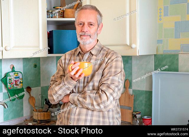 Mature man drinking his coffee in an orange cup, at morning in kitchen