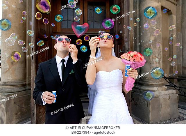 Bride and groom, bridal couple blowing bubbles, in front of St. Mary's Church, Krakow, Poland, Europe