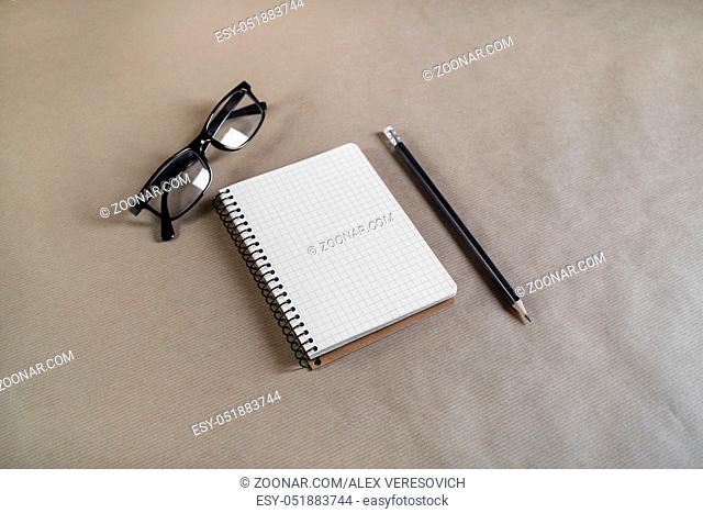 Photo of blank notebook, pencil and glasses on craft paper background