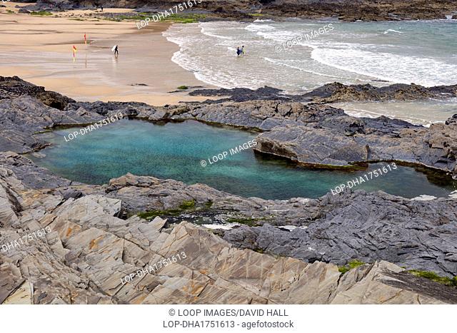 Large turquoise rock pool and coast with surfers on the beach