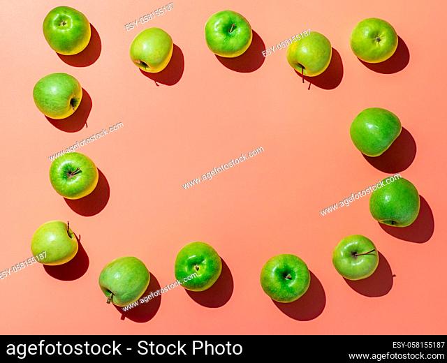 Green apples on orange or coral pink background with copy space for text or design in center, Colorful fruit frame. Flat lay or top view, Hard light