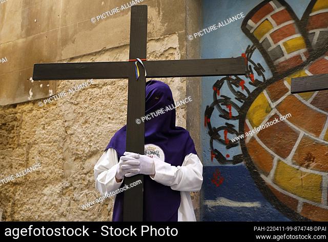 10 April 2022, Spain, Palma: A penitent wears a pointed cap, holds a cross and takes part in the Palm Sunday procession. The procession had been canceled since...