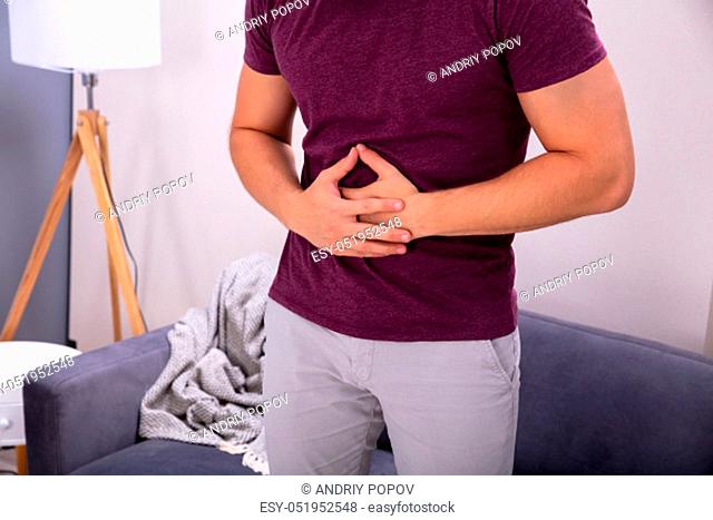 Midsection Of Man Suffering From Stomach Ache Standing Near Sofa