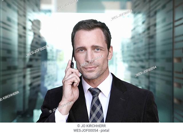 Germany, Cologne, Businessman standing in corridor using mobile phone, portrait