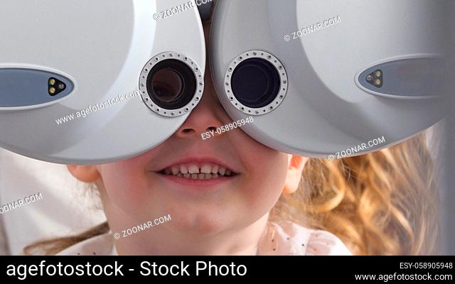 Ophthalmology clinic - smiling little blonde girl checks vision eyesight, close up, telephoto