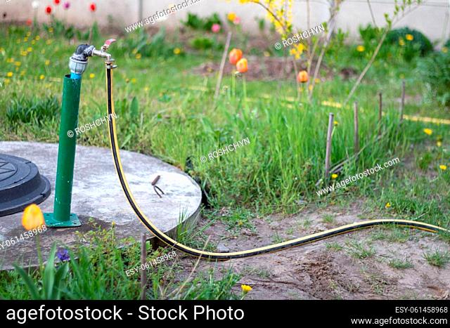Plumbing, water pump from a well. An outside water faucet with a yellow garden hose attached to it. Irrigation water pumping system for agriculture