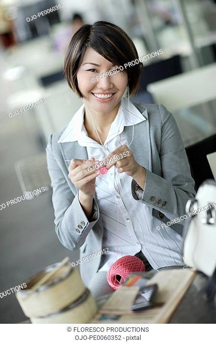 Businesswoman in cafeteria wearing ear buds and crocheting
