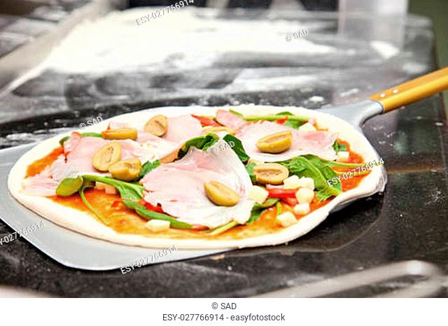 raw pizza with spinach, olives, ham
