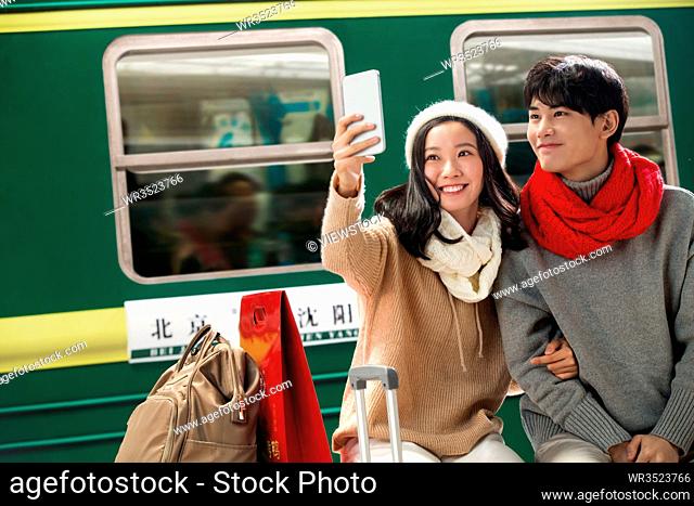 Young lovers see mobile phone in the railway station