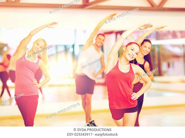 fitness, sport, training, gym and lifestyle concept - group of smiling people stretching in the gym