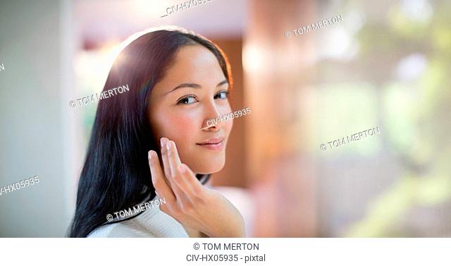 Portrait confident young woman applying moisturizer to face